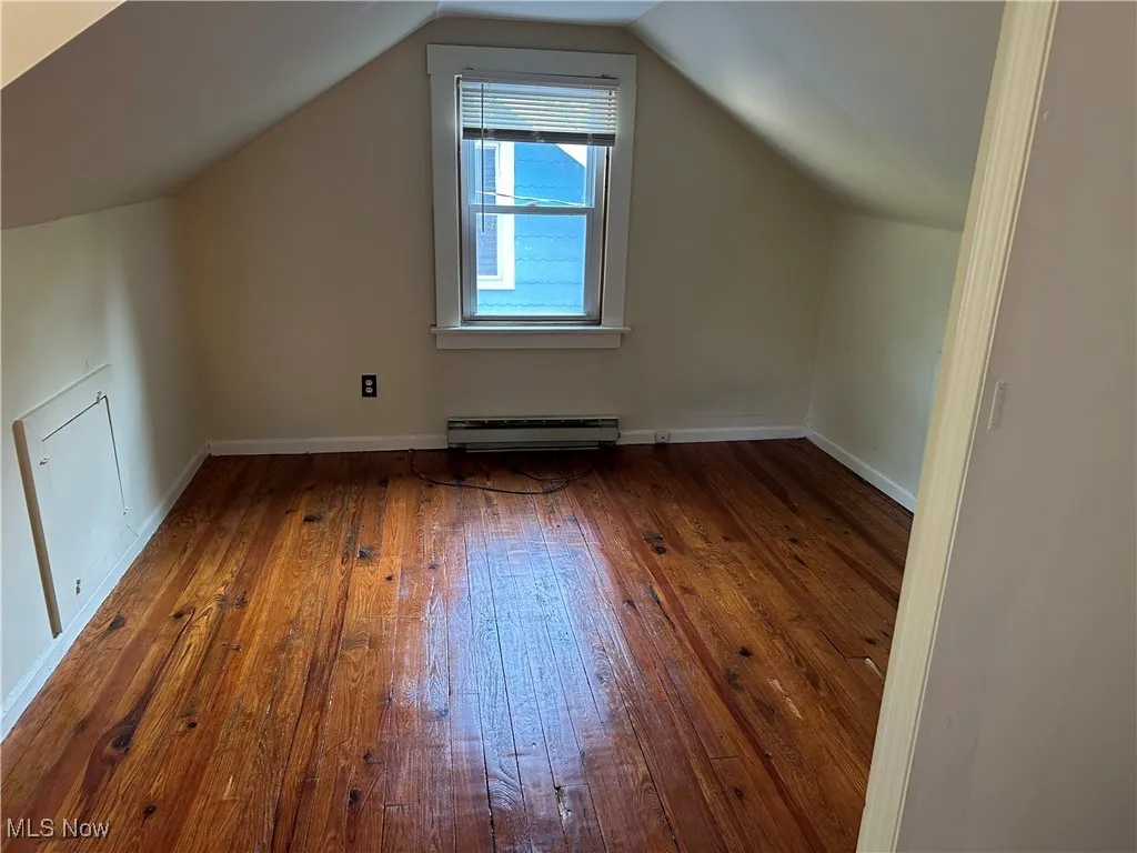 Additional living space with wood-type flooring, lofted ceiling, and a baseboard radiator