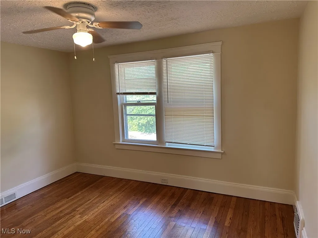 Empty room featuring healthy amount of natural light, hardwood / wood-style flooring, a ceiling fan, and a textured ceiling