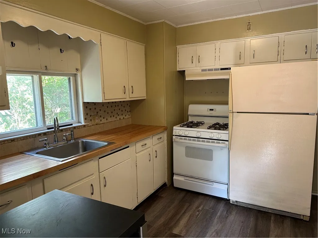 Kitchen with refrigerator, range, dark wood-style flooring, white cabinets, and ornamental molding