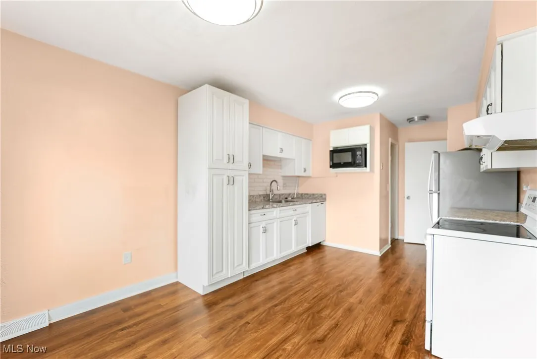 Kitchen featuring stove, wood finished floors, tasteful backsplash, exhaust hood, and black microwave