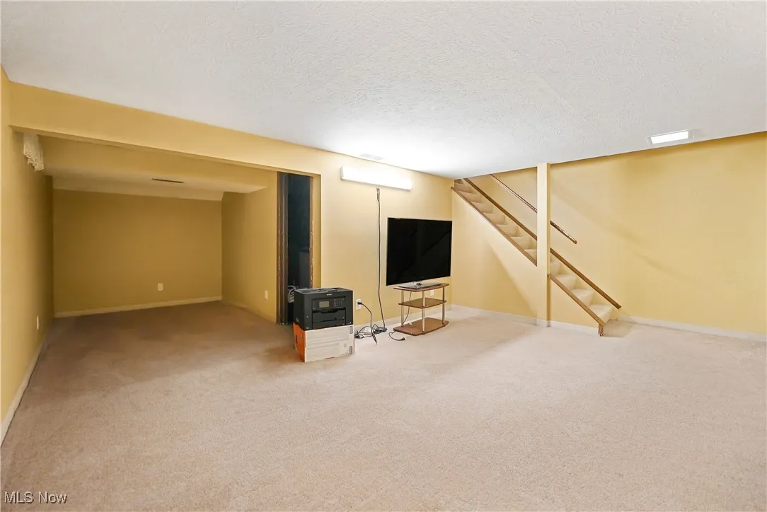 Finished below grade area with carpet floors, a textured ceiling, and stairway