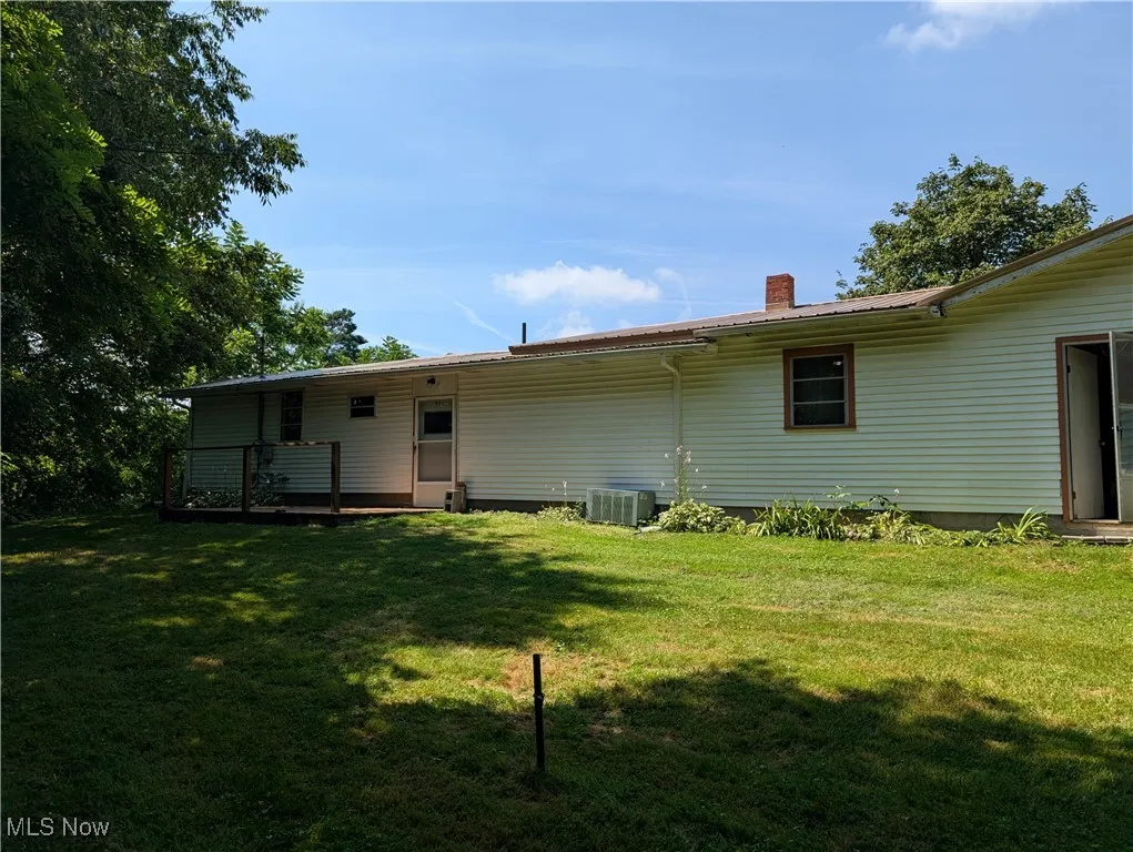 Rear view of property with a lawn, a chimney, a deck, and a metal roof
