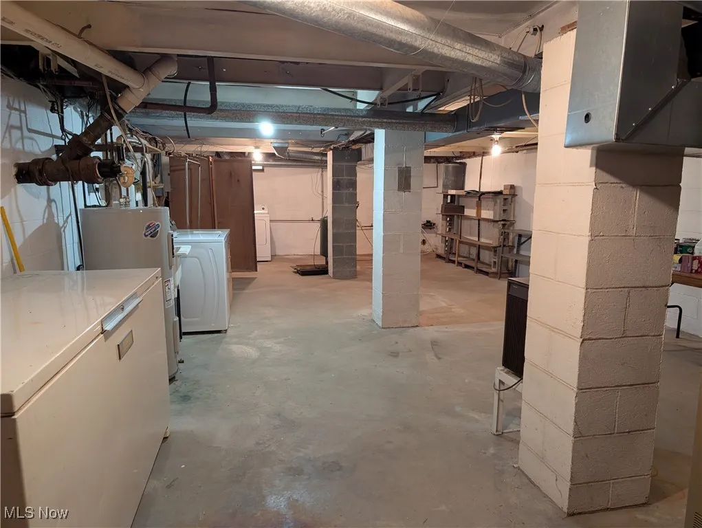 Unfinished below grade area featuring water heater, refrigerator, independent washer and dryer, and concrete block wall