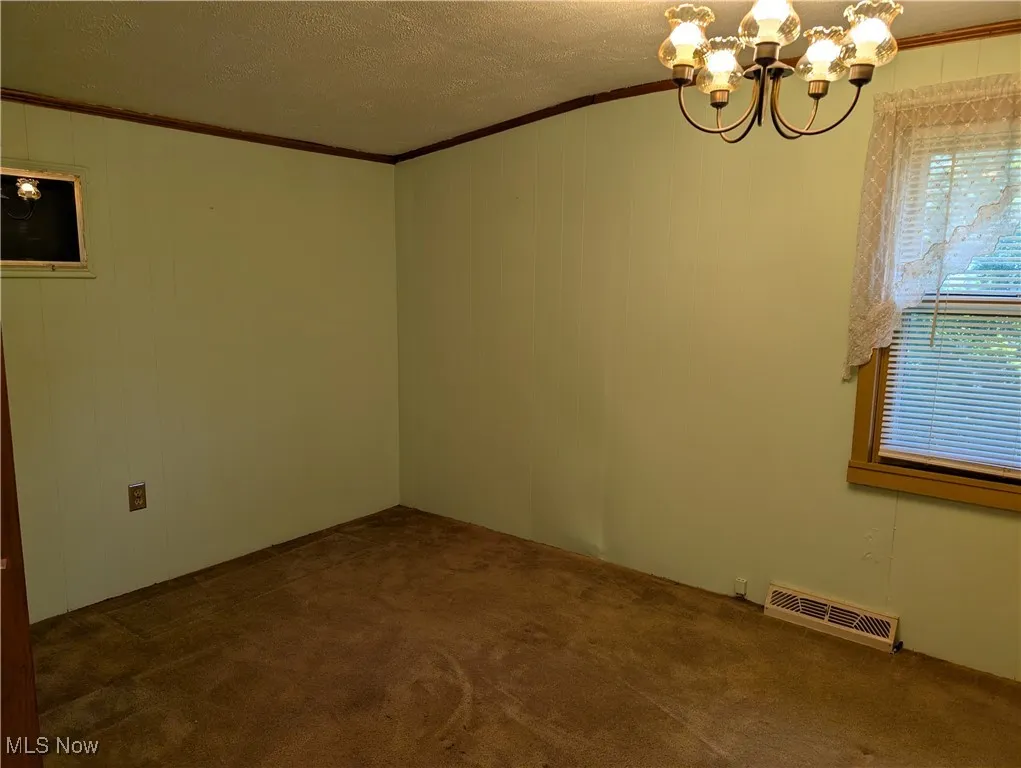 Spare room with ornamental molding, a chandelier, carpet floors, and a textured ceiling