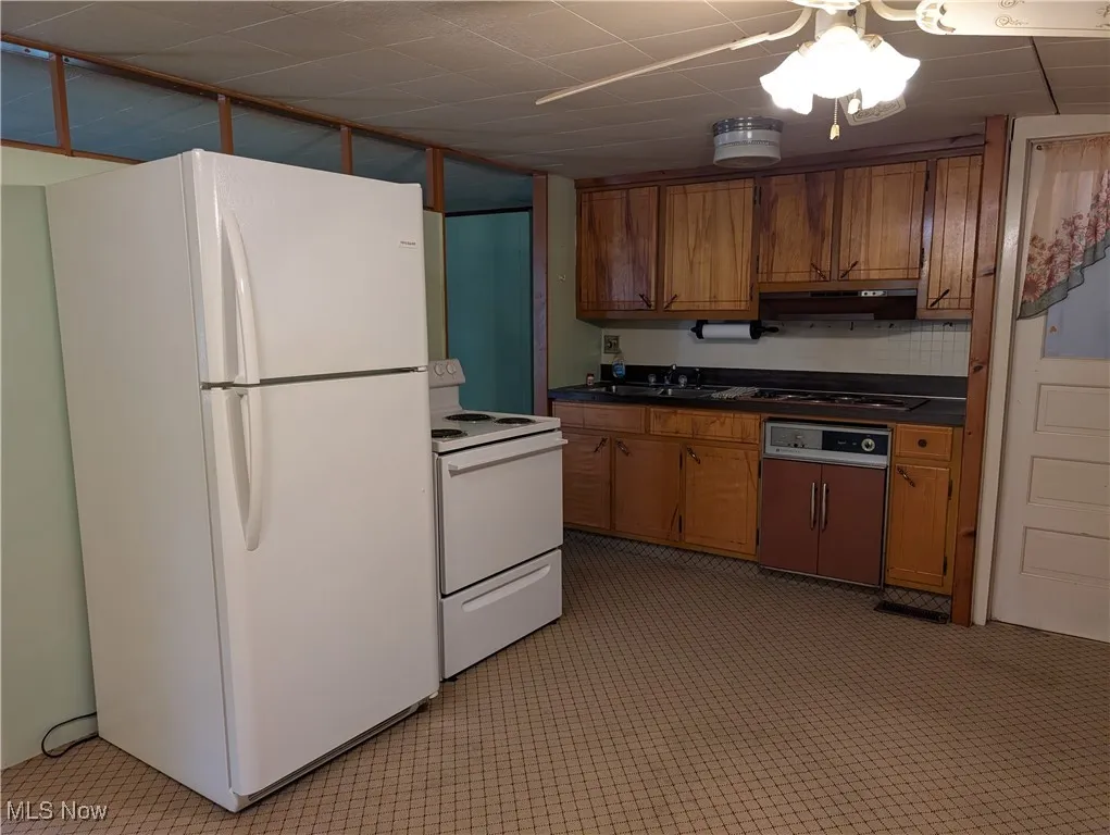 Kitchen featuring white appliances, brown cabinetry, and dark countertops