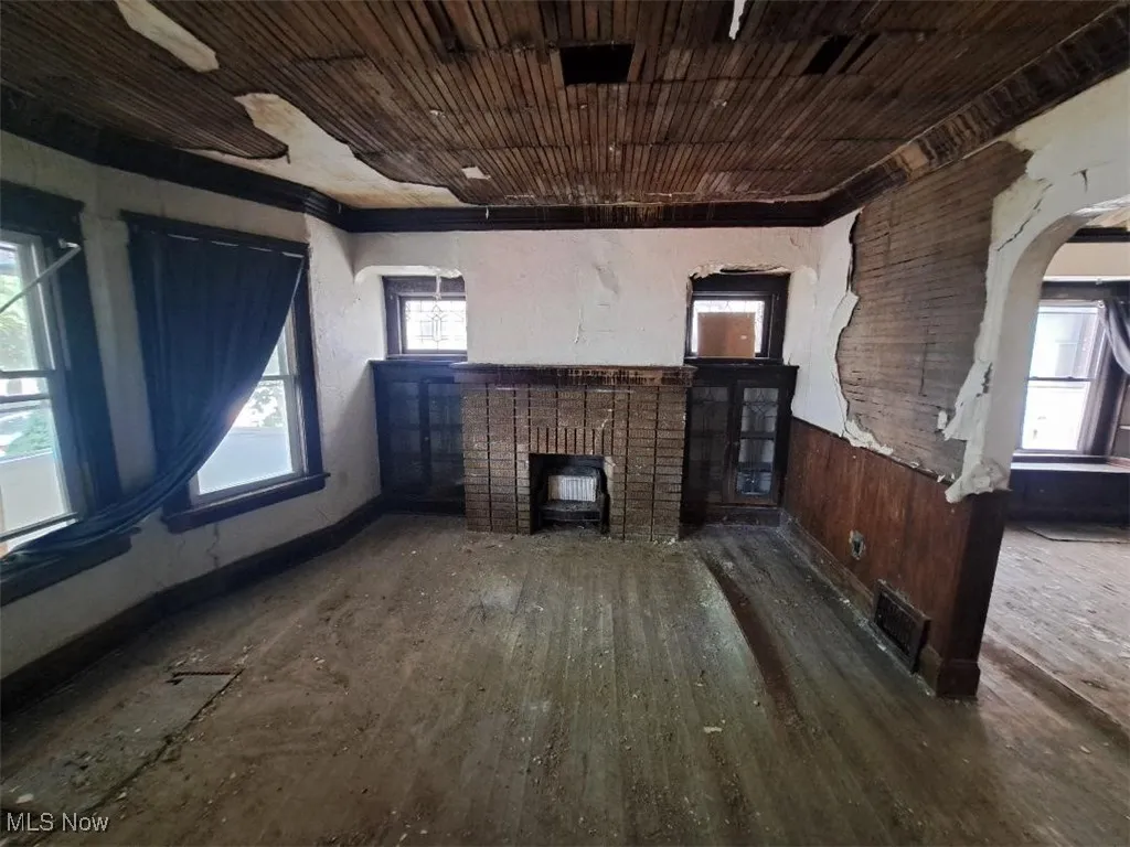 Unfurnished living room with a brick fireplace, arched walkways, and hardwood / wood-style flooring