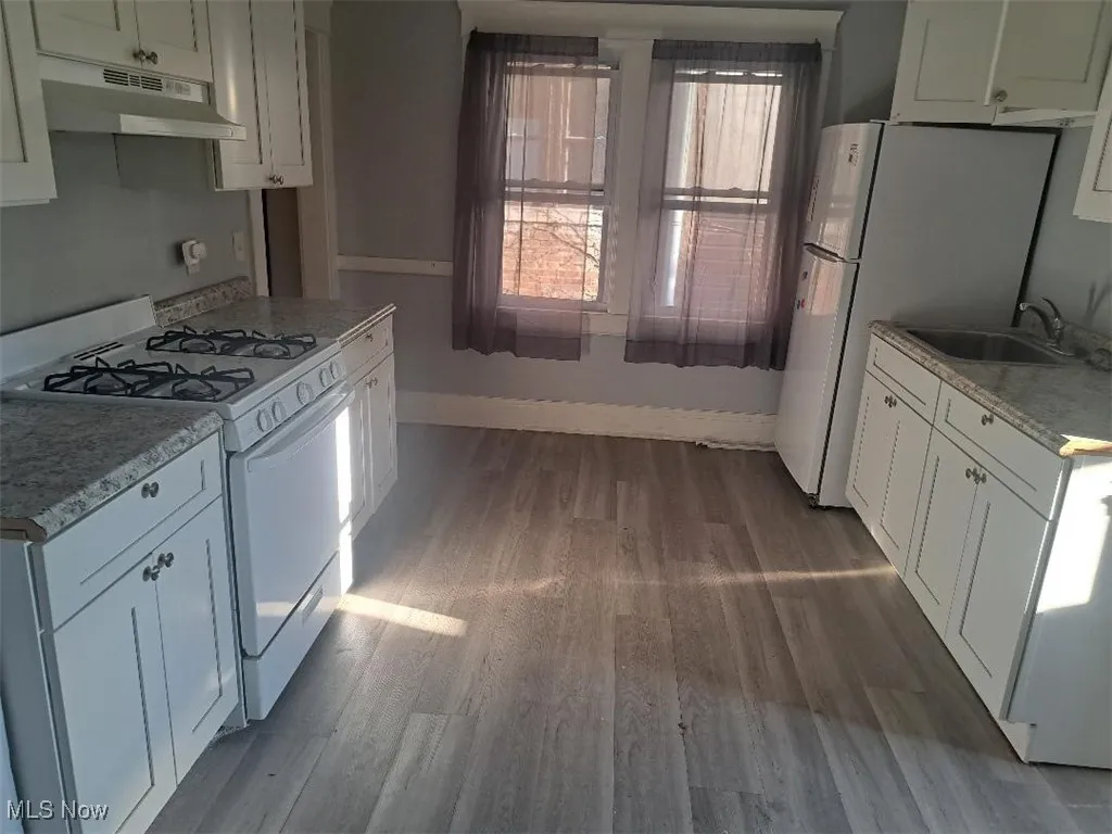 Kitchen with white appliances, under cabinet range hood, dark wood-style flooring, and white cabinets