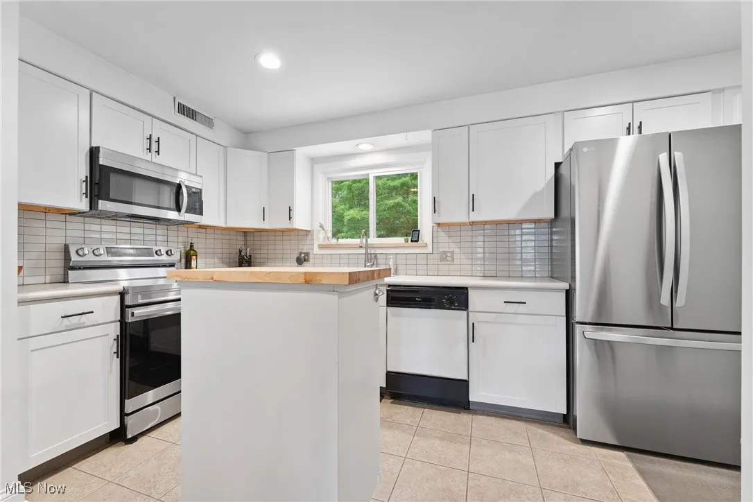 Kitchen with appliances with stainless steel finishes, light tile patterned floors, a center island, white cabinetry, and tasteful backsplash