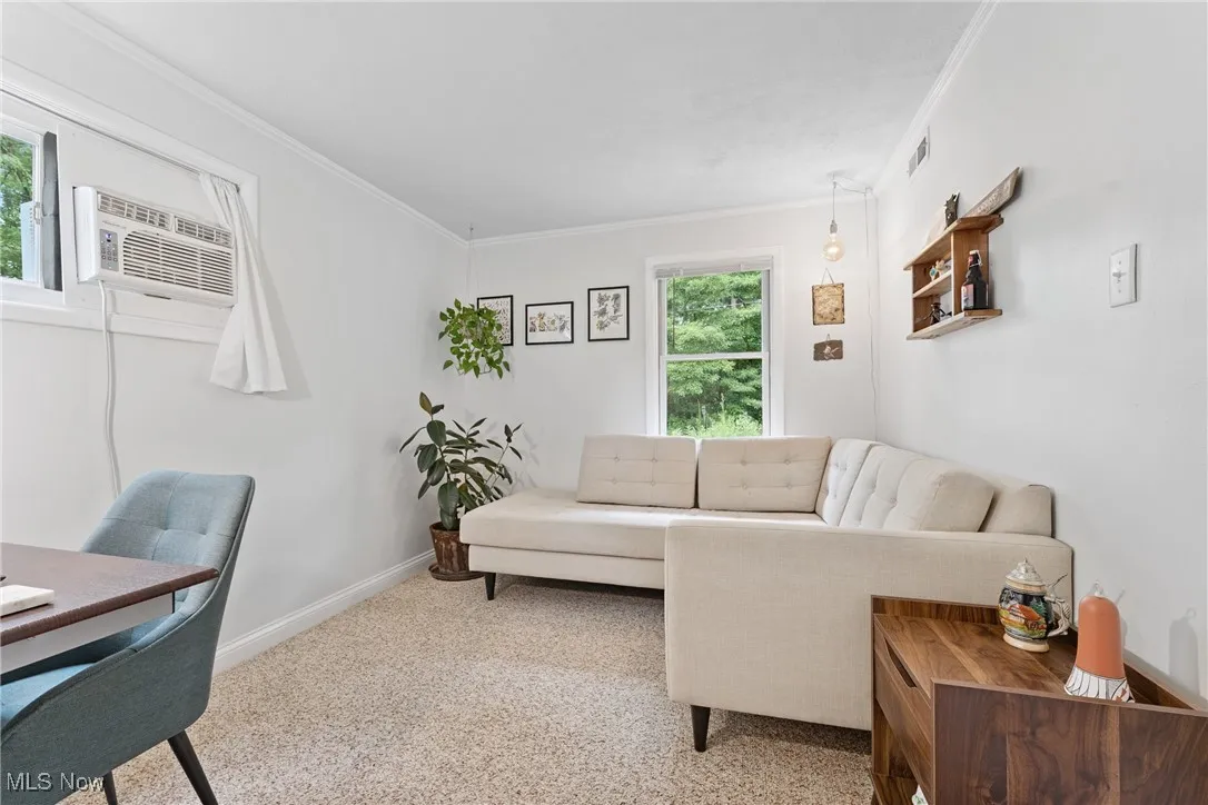 Carpeted living room with ornamental molding and an AC wall unit