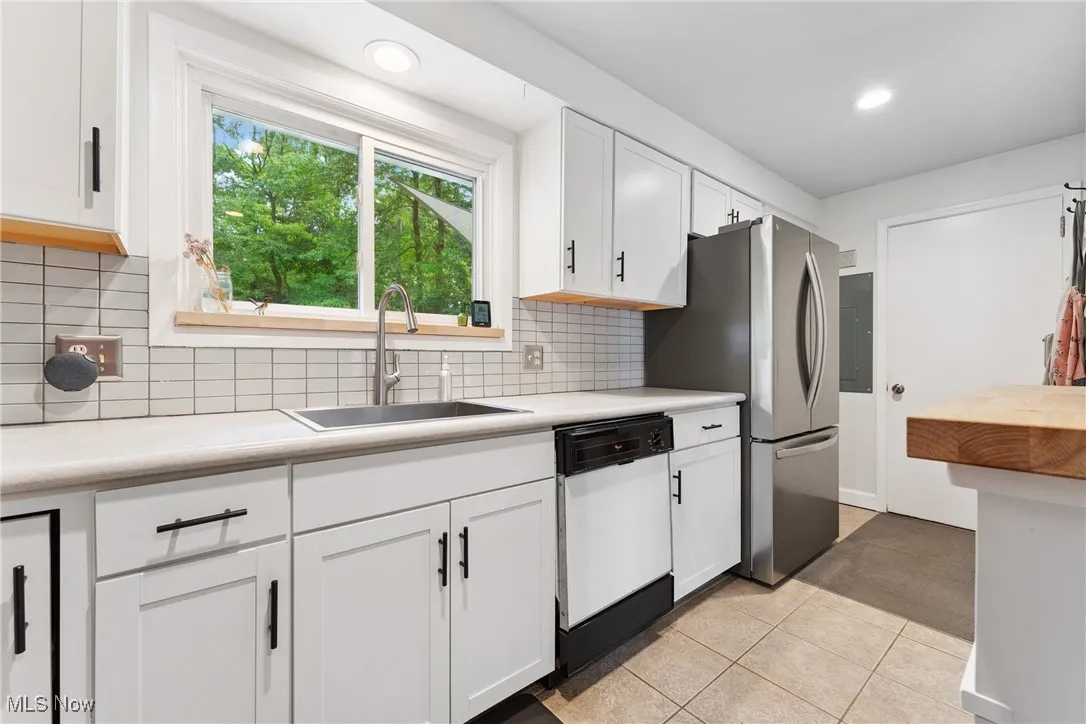 Kitchen with dishwasher, light countertops, freestanding refrigerator, white cabinetry, and recessed lighting