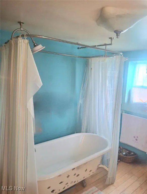Full bathroom with wood finished floors and shower / bath combo with shower curtain