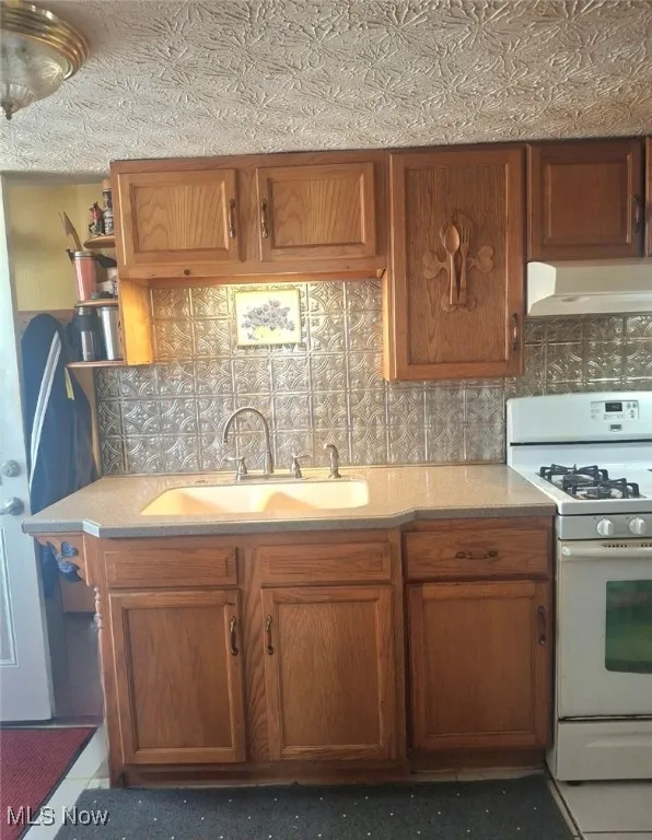 Kitchen featuring white range with gas cooktop, custom exhaust hood, open shelves, and light countertops