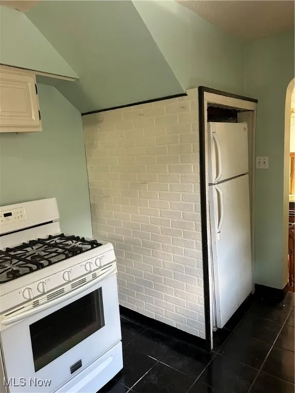 Kitchen featuring stove, refrigerator, dark tile patterned flooring, and white cabinetry