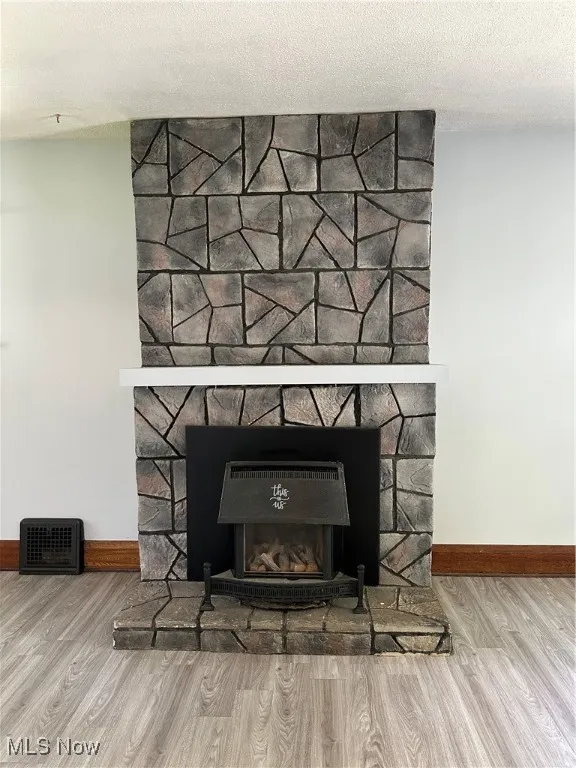 Detailed view of a fireplace, wood finished floors, and a textured ceiling