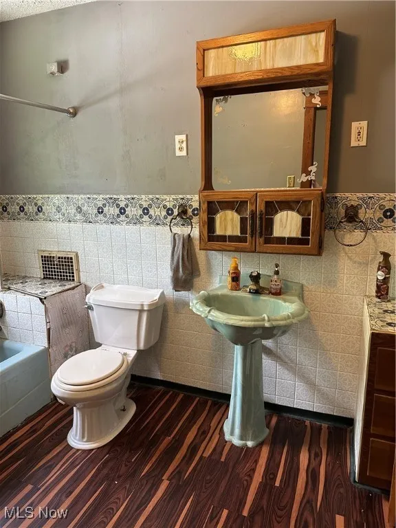 Full bath featuring tile walls, wood finished floors, a tub to relax in, and a wainscoted wall