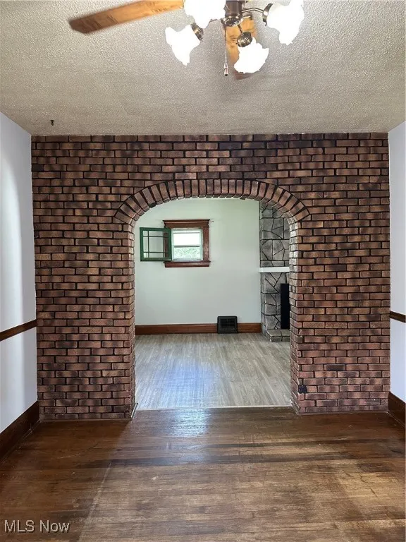 Unfurnished living room featuring hardwood / wood-style floors, a textured ceiling, a fireplace, brick wall, and arched walkways
