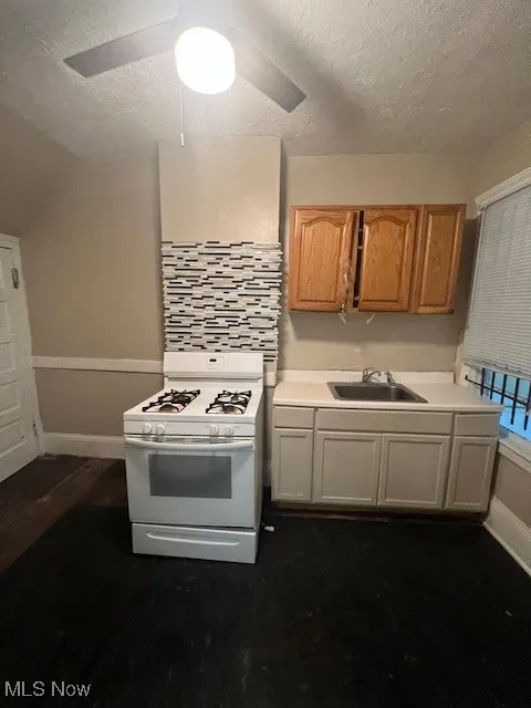 Kitchen featuring stove, light countertops, a textured ceiling, ceiling fan, and dark wood-style flooring