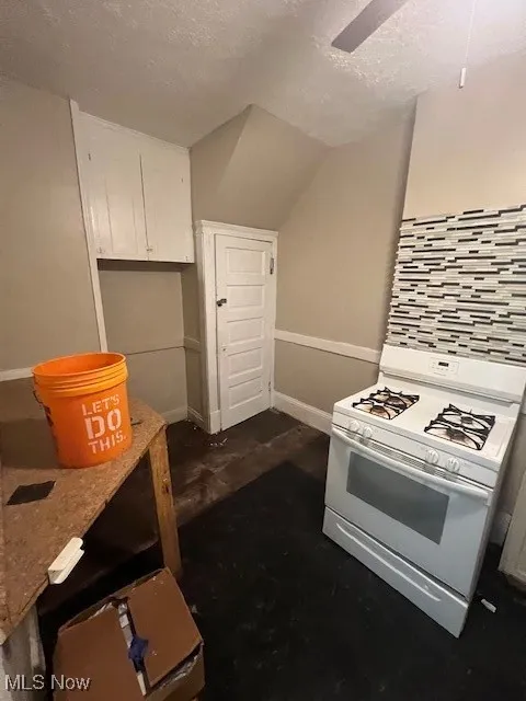 Kitchen featuring stove, a textured ceiling, white cabinetry, and tasteful backsplash