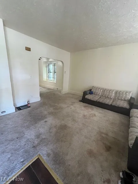 Unfurnished living room featuring arched walkways, carpet floors, and a textured ceiling