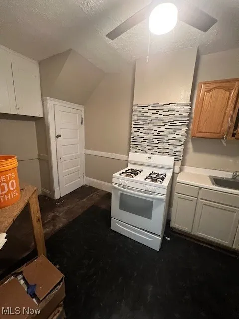 Kitchen with stove, light countertops, a ceiling fan, a textured ceiling, and decorative backsplash