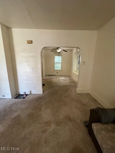 Unfurnished living room with arched walkways, carpet, and ceiling fan