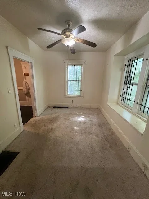 Carpeted spare room featuring a textured ceiling and ceiling fan
