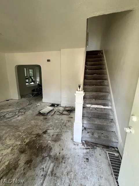Stairs with arched walkways and hardwood / wood-style flooring