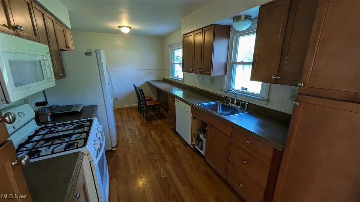 Kitchen featuring white appliances, dark countertops, dark wood-style flooring, and a wainscoted wall