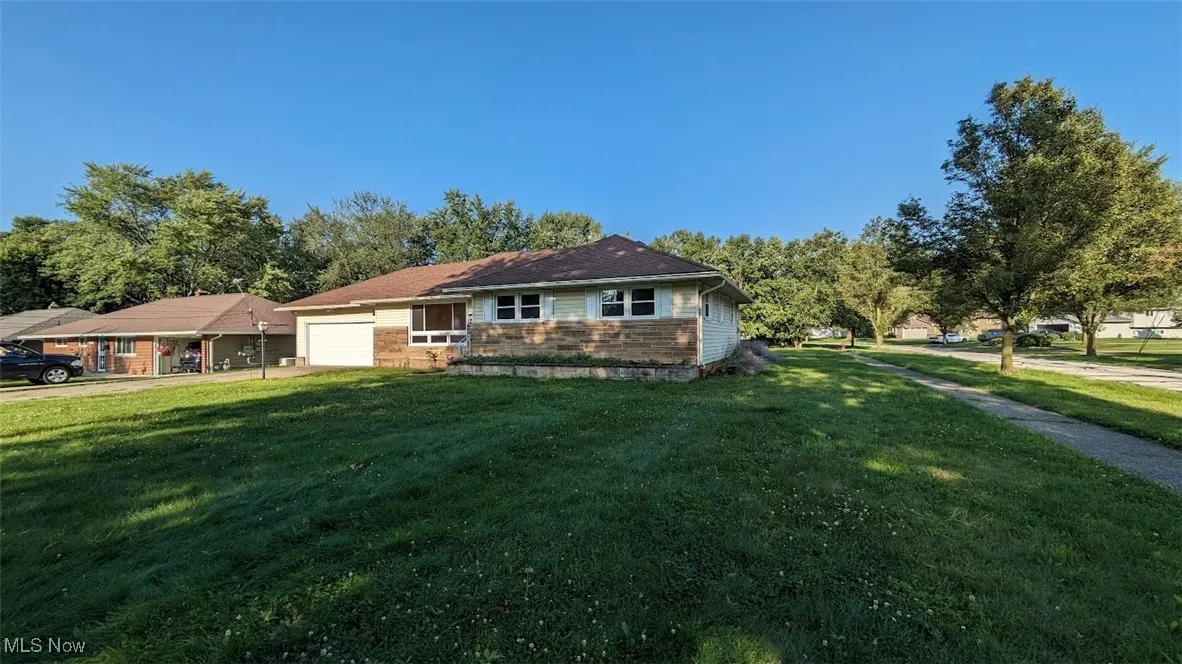 View of front of property featuring a garage, a front lawn, and stone siding