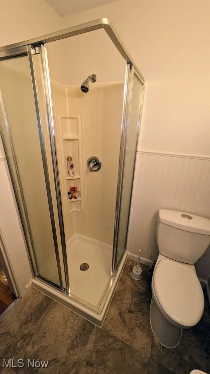 Full bathroom featuring a wainscoted wall and a stall shower