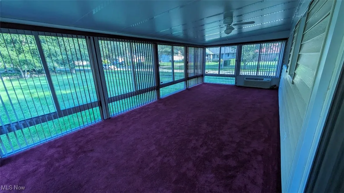 Unfurnished sunroom featuring a ceiling fan and a wall unit AC