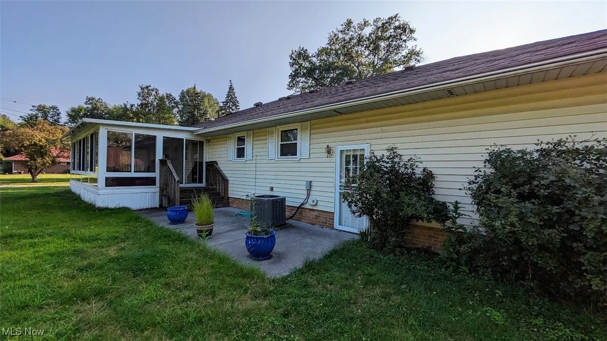 Back of property with a sunroom, a lawn, and a patio