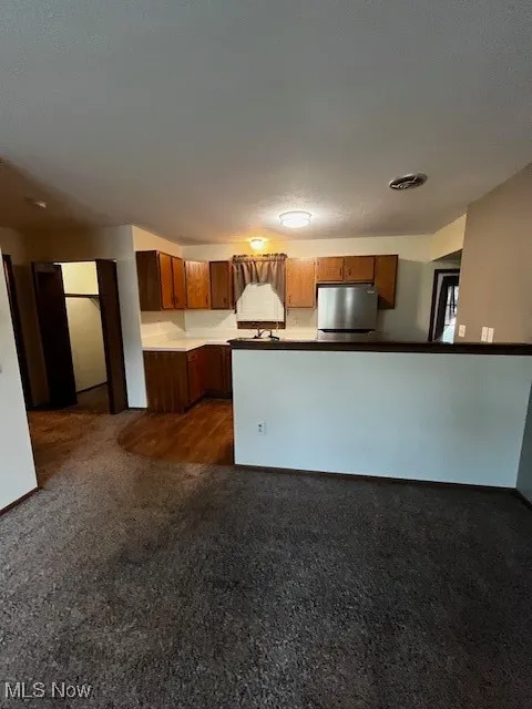 Kitchen with dark carpet, brown cabinets, fridge, and a peninsula
