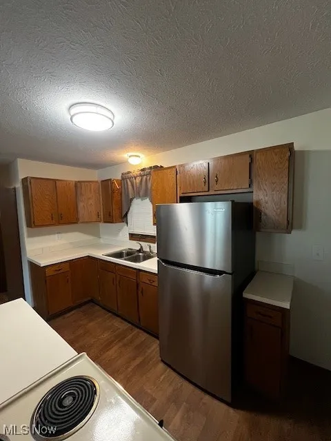 Kitchen featuring brown cabinetry, dark wood finished floors, fridge, a textured ceiling, and light countertops