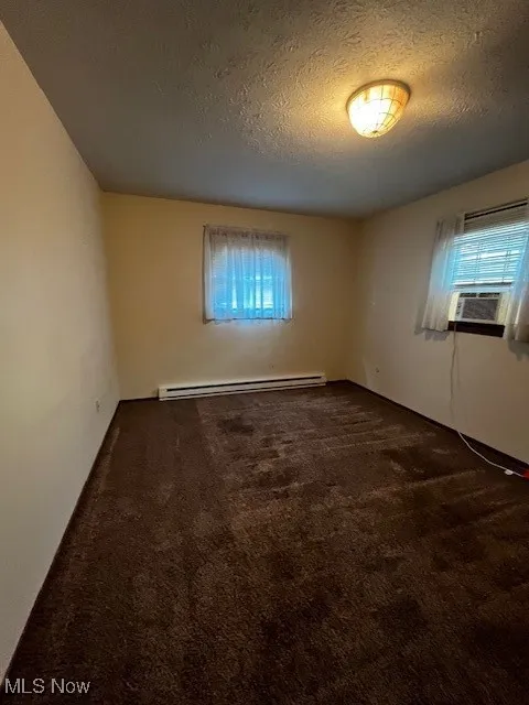 Empty room with carpet flooring, a textured ceiling, and a baseboard heating unit