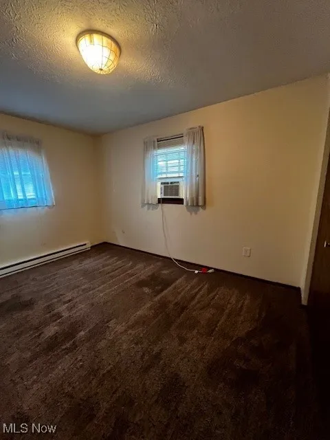 Spare room with dark carpet, baseboard heating, a textured ceiling, and cooling unit