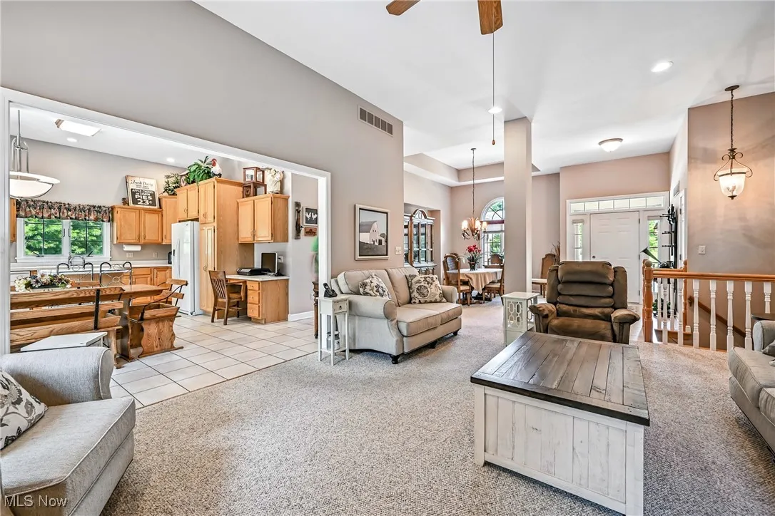 Living room featuring light colored carpet, ceiling fan, a chandelier, a towering ceiling, and recessed lighting