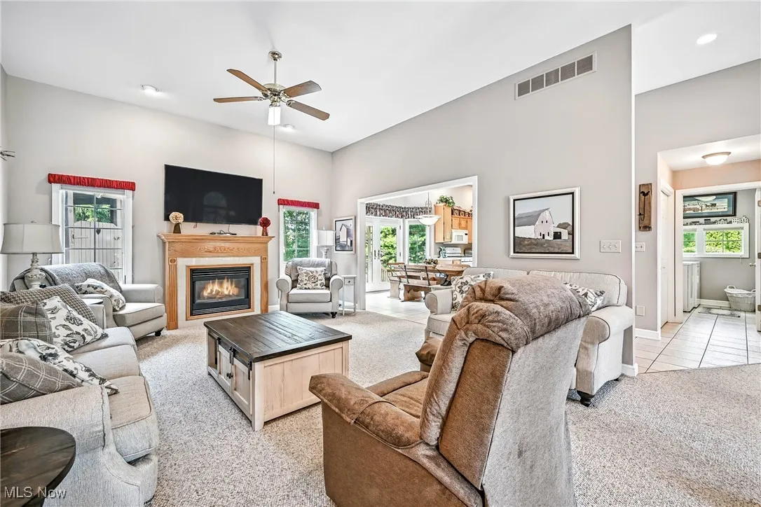 Living room with ceiling fan, healthy amount of natural light, a high ceiling, light colored carpet, and a glass covered fireplace