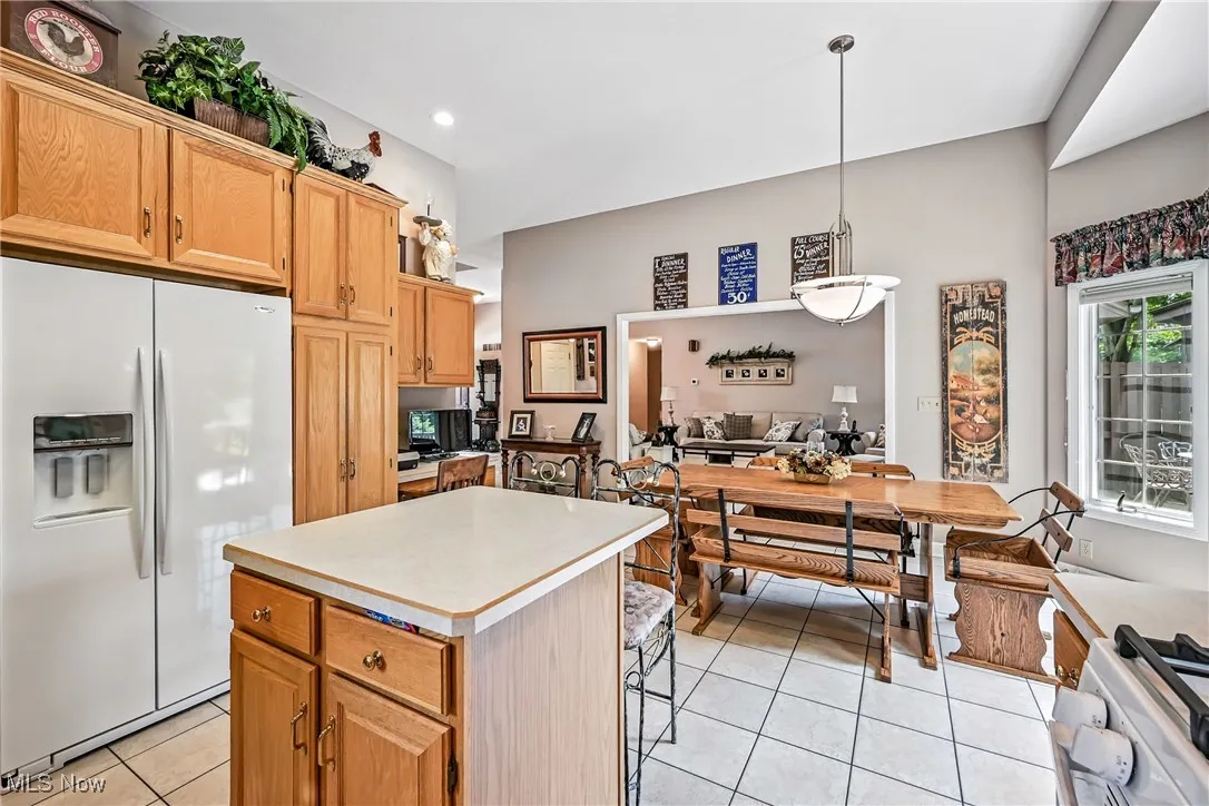 Kitchen with white refrigerator with ice dispenser, light tile patterned floors, a center island, light countertops, and decorative light fixtures