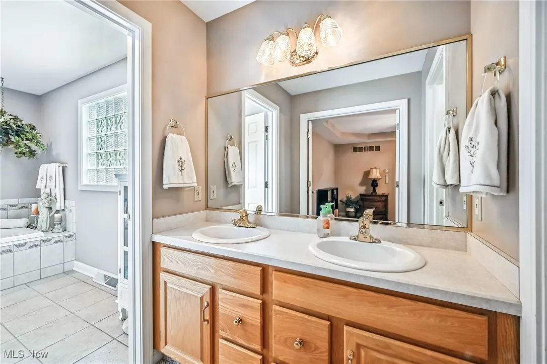 Bathroom with double vanity, tile patterned floors, and a relaxing tiled tub