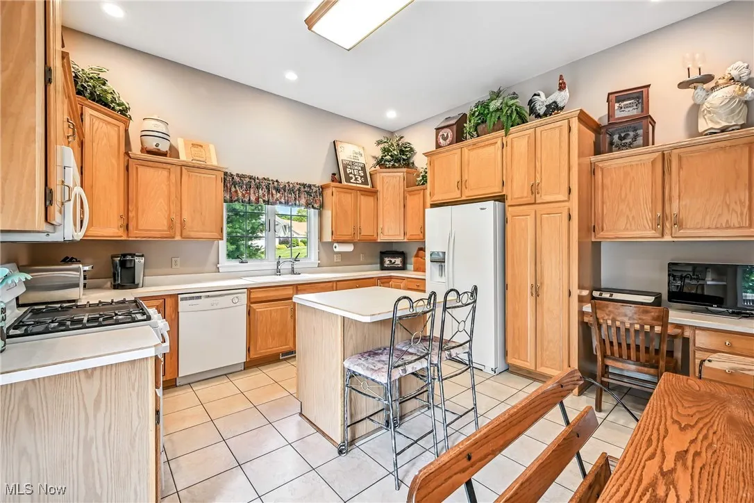 Kitchen with white appliances, light countertops, a kitchen island, a kitchen breakfast bar, and light tile patterned floors