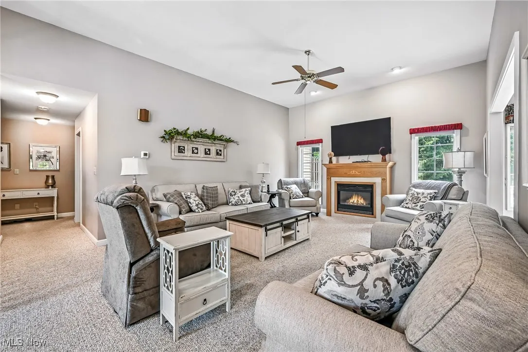 Living area with carpet, a ceiling fan, and a glass covered fireplace