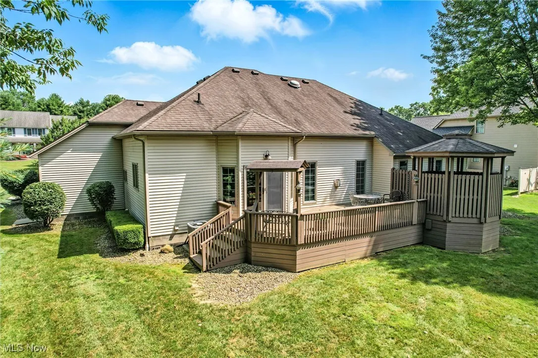 Rear view of house featuring a gazebo, a shingled roof, a lawn, and a wooden deck