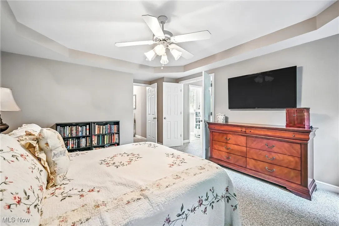 Carpeted bedroom featuring a ceiling fan and a tray ceiling