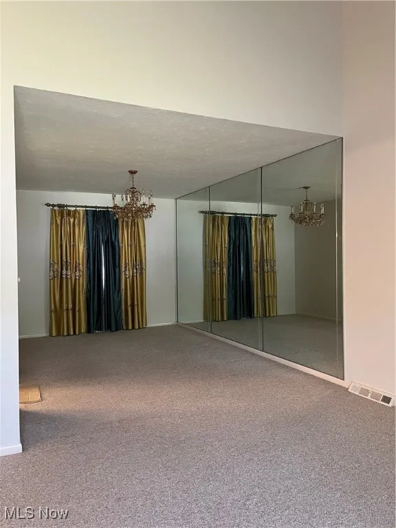 Carpeted empty room featuring a chandelier