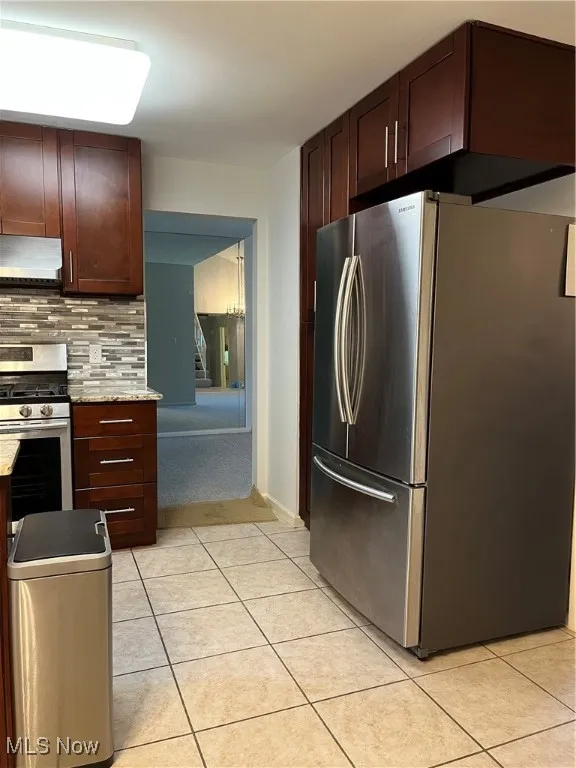 Kitchen with refrigerator, stove, decorative backsplash, range hood, and light tile patterned flooring