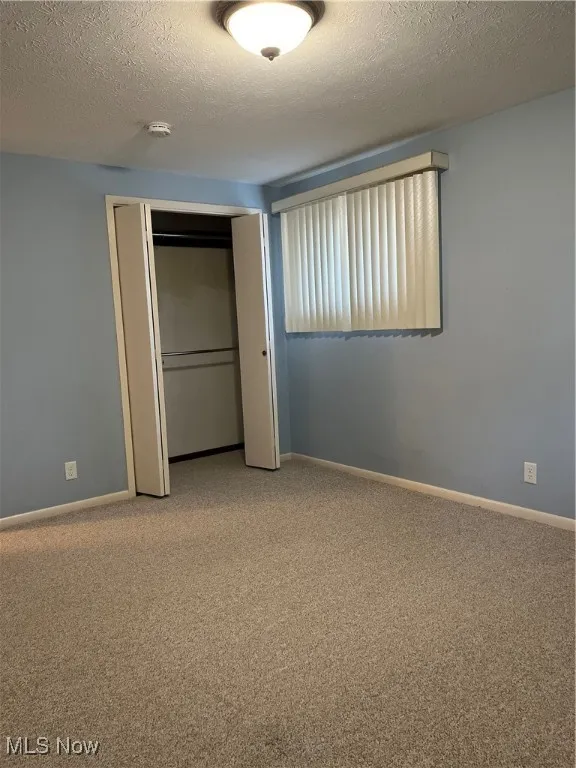 Unfurnished bedroom with light carpet, a closet, and a textured ceiling