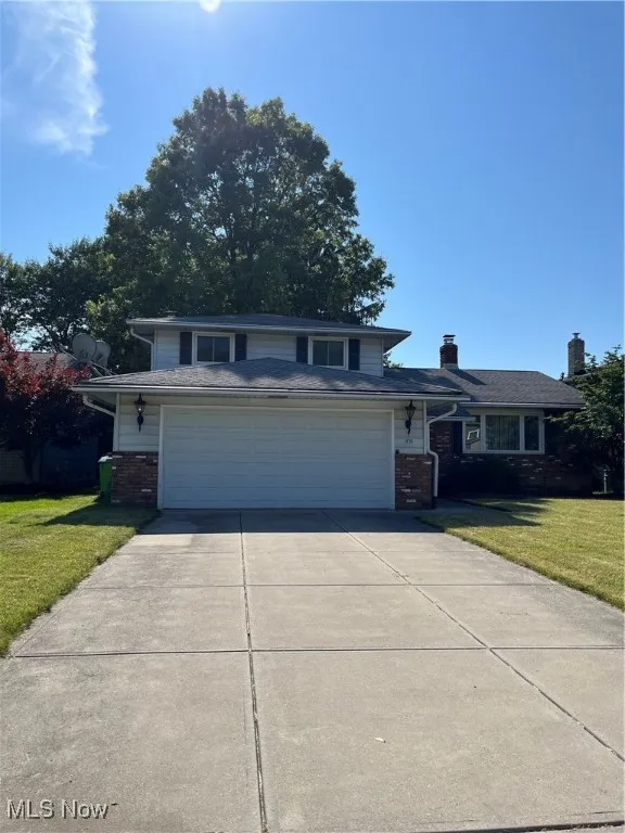 View of front of home with brick siding, concrete driveway, a front lawn, and an attached garage
