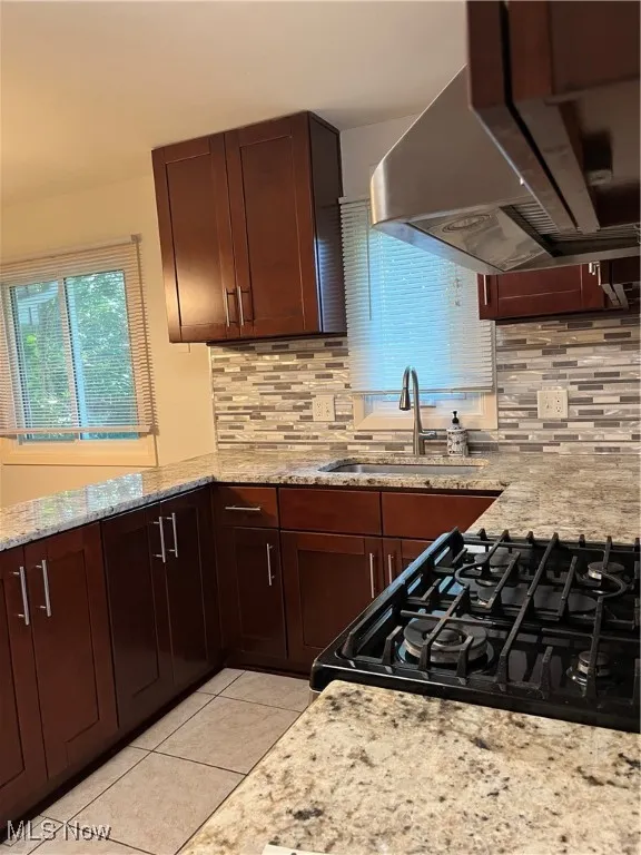 Kitchen featuring stove, extractor fan, backsplash, and light tile patterned floors