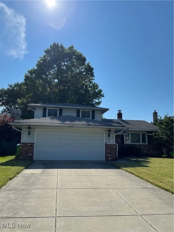 View of front of house featuring brick siding, driveway, a front yard, and a chimney